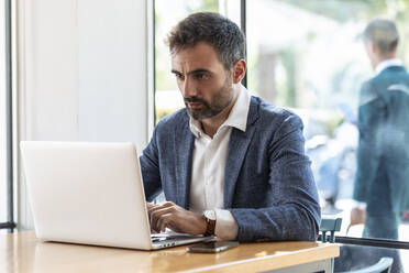 Businessman using laptop while sitting at table in cafe - JSRF01036