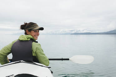 Happy female woman sea kayaking pristine waters of Muir Inlet in Glacier Bay National Park and Preserve Alaska - MINF15055