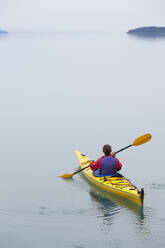 Female sea kayaker paddling pristine waters of Muir Inlet overcast sky in distance Glacier Bay National Park Alaska - MINF15058