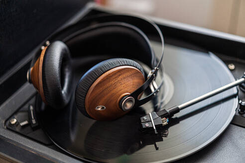 Vintage-Kopfhörer aus Holz liegen auf einem schwarzen Vinyl in einem Plattenspieler - ADSF10995