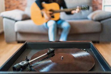 Anonyme Frau, die zu Hause auf ihrer Couch Gitarre spielt und mit Online-Unterricht neben einem Plattenspieler lernt. - ADSF11000