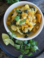 Von oben Teller mit köstlichem vegetarischem Curry und Limettenscheiben auf einem Tablett auf Holzuntergrund - ADSF11018