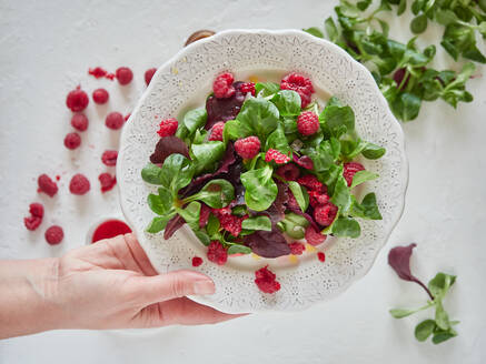 Person mit Teller mit Himbeer- und Spinatsalat - ADSF11021