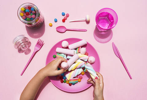 Hände eines kleinen Mädchens, das Süßigkeiten von einem Plastikteller aufhebt - GEMF04067