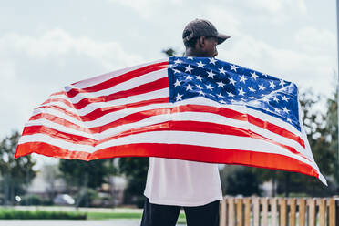 Ernster afroamerikanischer Mann, der die amerikanische Flagge auf der Schulter hält und wegschaut - ADSF11141