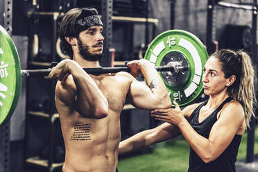 Starker Trainer in Sportkleidung hilft einem sportlichen Kunden beim Langhanteltraining in einem modernen Fitnessstudio - ADSF11172