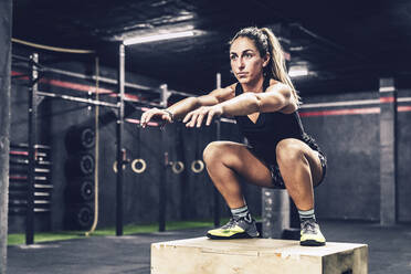 Sportliche Frau springt auf einen Kasten, um ihre Ausdauer im Fitnessstudio zu verbessern - ADSF11176