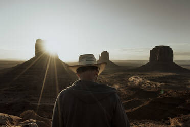 Rückansicht eines Touristen mit Hut, der alte Gebäude in der Wüste im Sonnenlicht in den USA betrachtet - ADSF11184