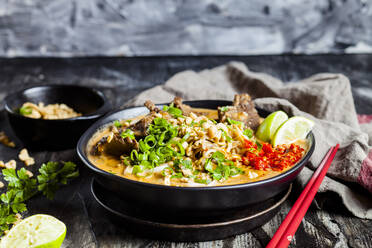 Schale mit roter Currysuppe mit Reisnudeln, Rindfleisch, Gemüse, Frühlingszwiebeln, Erdnüssen und Limette - SBDF04315