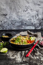 Schale mit roter Currysuppe mit Reisnudeln, Rindfleisch, Gemüse, Frühlingszwiebeln, Erdnüssen und Limette - SBDF04316