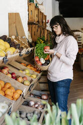 Frau kauft in einem Geschäft ein, während sie einen Korb hält und einen Apfel betrachtet - RDGF00061