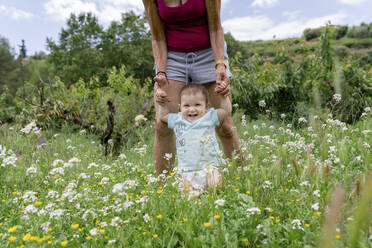 Cheerful granddaughter holding hands with grandmother in field - GEMF04073
