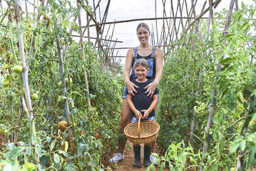 Mutter und Tochter mit Weidenkorb im Gewächshaus mit Tomatenpflanzen - VEGF02673