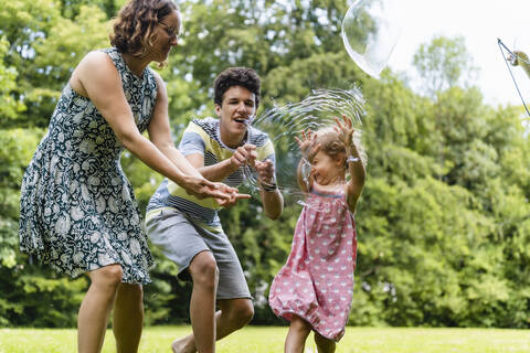 Glückliche Familie beim Platzen einer Seifenblase im Park, lizenzfreies Stockfoto