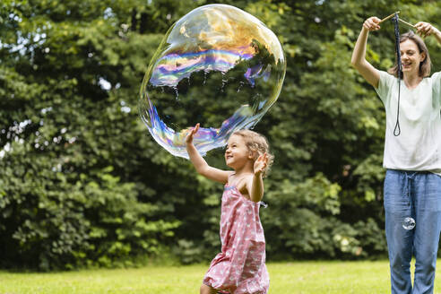 Mother and daughter playing with bubble at park - DIGF12908