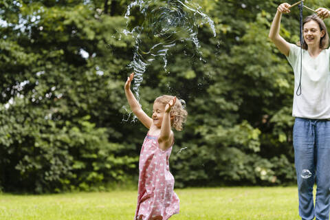 Mädchen lässt Seifenblase platzen, während sie sich im öffentlichen Park vergnügt, lizenzfreies Stockfoto