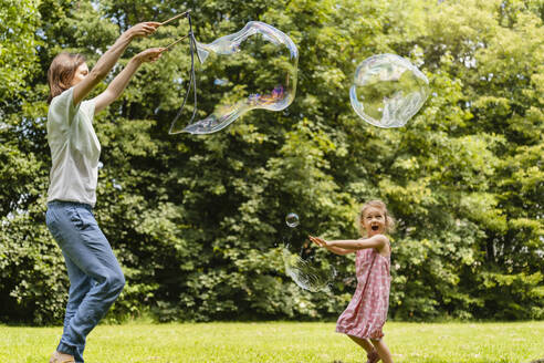 Happy daughter exploding bubble with mother at park - DIGF12913