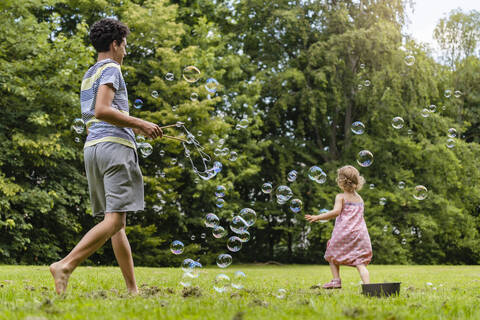 Bruder und Schwester spielen mit Seifenblasen im Park, lizenzfreies Stockfoto