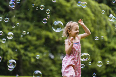 Fröhliches Mädchen läuft inmitten von Seifenblasen im Park - DIGF12917