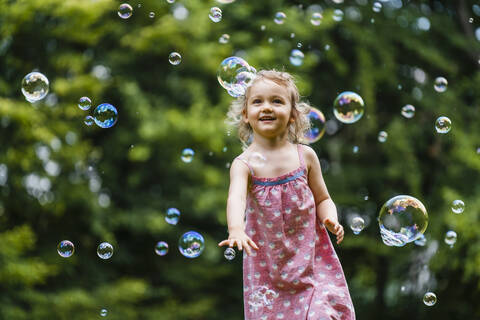Happy girl enjoying while running amidst bubbles at park stock photo