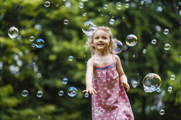 Glückliches Mädchen genießt beim Laufen inmitten von Seifenblasen im Park - DIGF12918