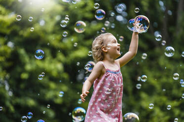 Cheerful girl amidst bubbles at park - DIGF12919