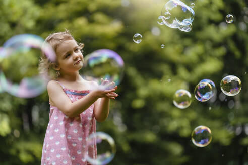 Cute girl looking at bubbles while standing in park - DIGF12922