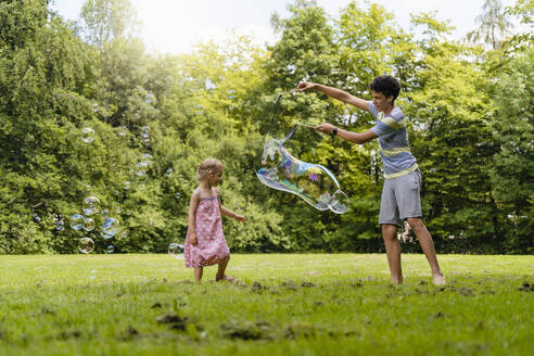 Brother making bubble for sister at park - DIGF12923