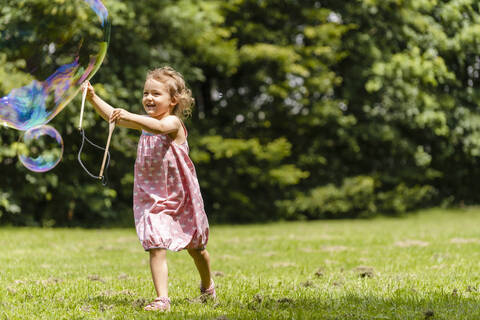 Lächelndes Mädchen läuft mit Seifenblasenstab im Park, lizenzfreies Stockfoto