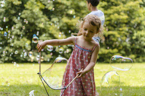 Cute baby girl making bubble with brother in background at park stock photo