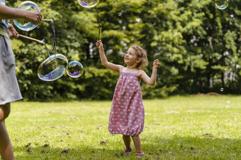 Cute girl exploding bubble with stick by brother at park stock photo