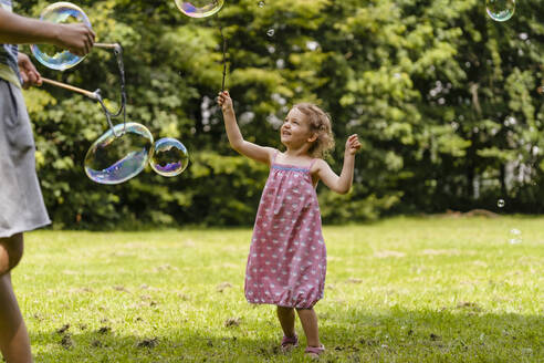 Cute girl exploding bubble with stick by brother at park - DIGF12926