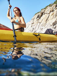 Woman wearing bikini kayaking in boat against clear blue sky - VEGF02702