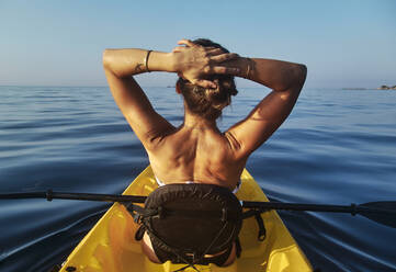 Frau mit Händen hinter dem Kopf sitzt in Boot gegen klaren blauen Himmel - VEGF02705