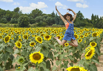 Happy woman jumping in sunflower field during summer - VEGF02710