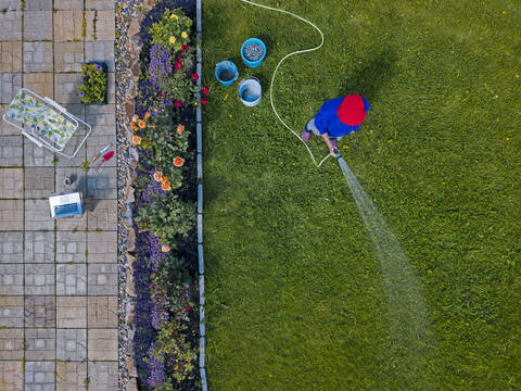 Luftaufnahme einer erwachsenen Frau beim Bewässern von Gras im Hinterhof, lizenzfreies Stockfoto