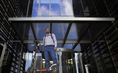 Businessman with electric push scooter standing against building - VEGF02723