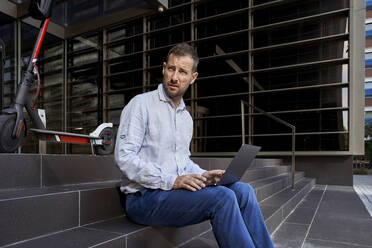 Businessman with laptop looking away while sitting on staircase - VEGF02726