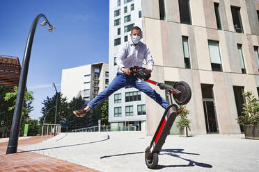 Entrepreneur jumping while holding electric push scooter in city during sunny day - VEGF02752