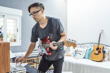 Musician with guitar using laptop at home - DLTSF01087