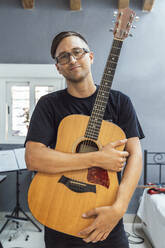 Selbstbewusster Musiker, der seine Gitarre zu Hause an die Wand hält - DLTSF01091