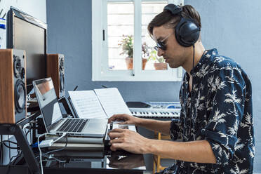 Man with headphones using laptop and keyboard at home - DLTSF01107