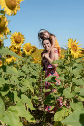 Lächelnde Mutter trägt Tochter auf den Schultern in einem Sonnenblumenfeld - GEMF04089