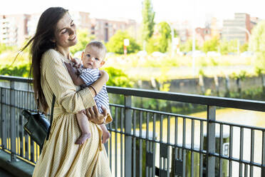 Mother holding her baby boy on a bridge - IHF00385