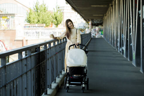 Lächelnde Mutter mit einem Kinderwagen auf einer Brücke - IHF00388