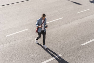 Man using mobile phone while crossing street in city - UUF20864