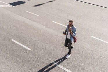 Smiling man talking on mobile phone while crossing street in city - UUF20865