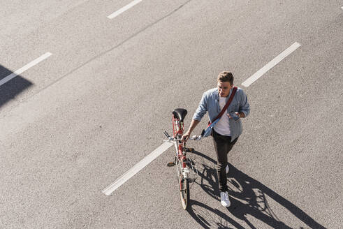 Junger Mann überquert Straße mit Fahrrad in der Stadt - UUF20866