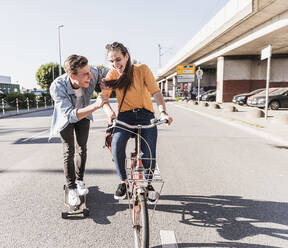 Playful boyfriend skateboarding while girlfriend riding bicycle on street in city - UUF20877