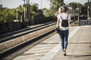 Woman with skateboard walking on railroad station platform - UUF20891